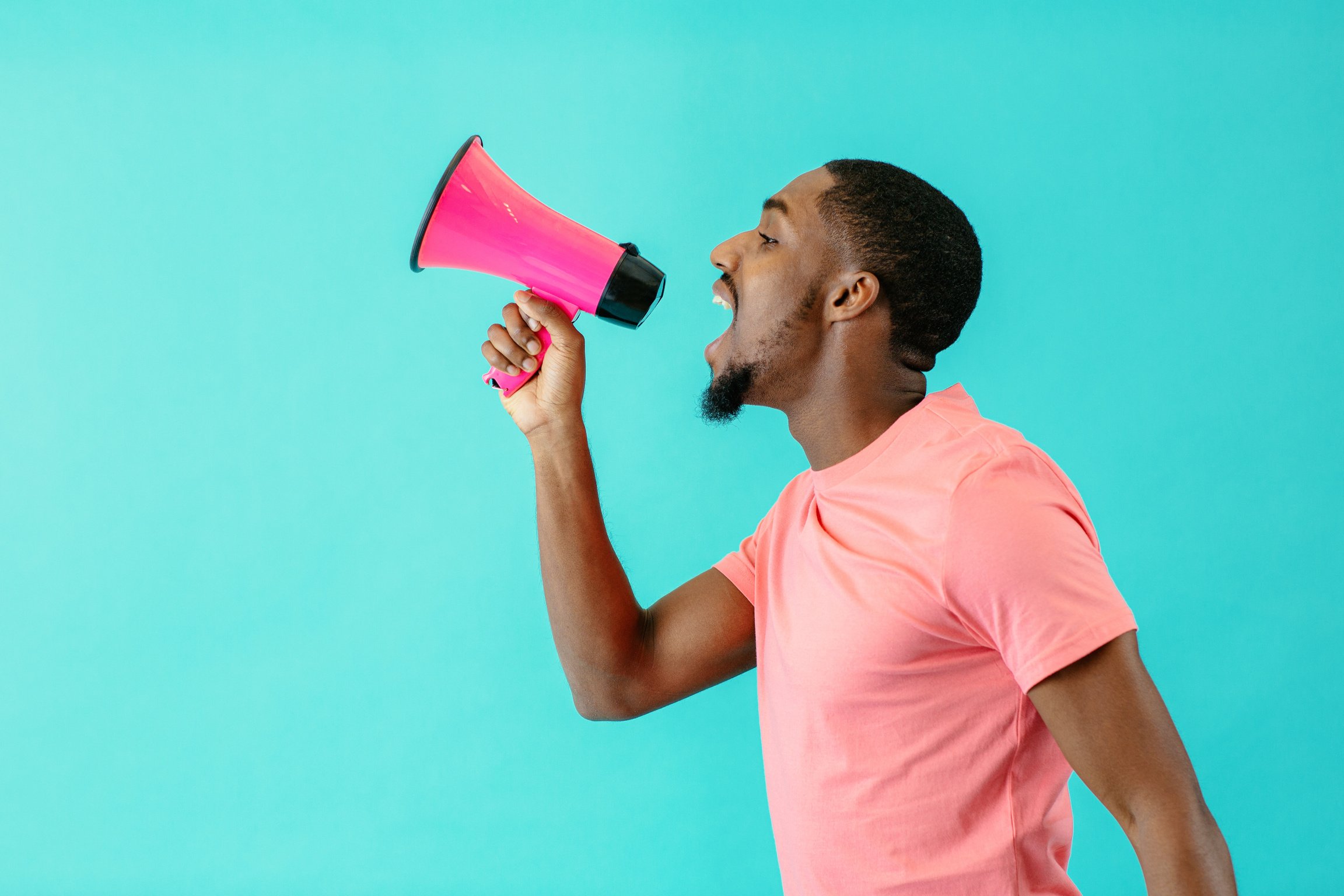 Portrait of a young man shouting through megaphone with mouth open